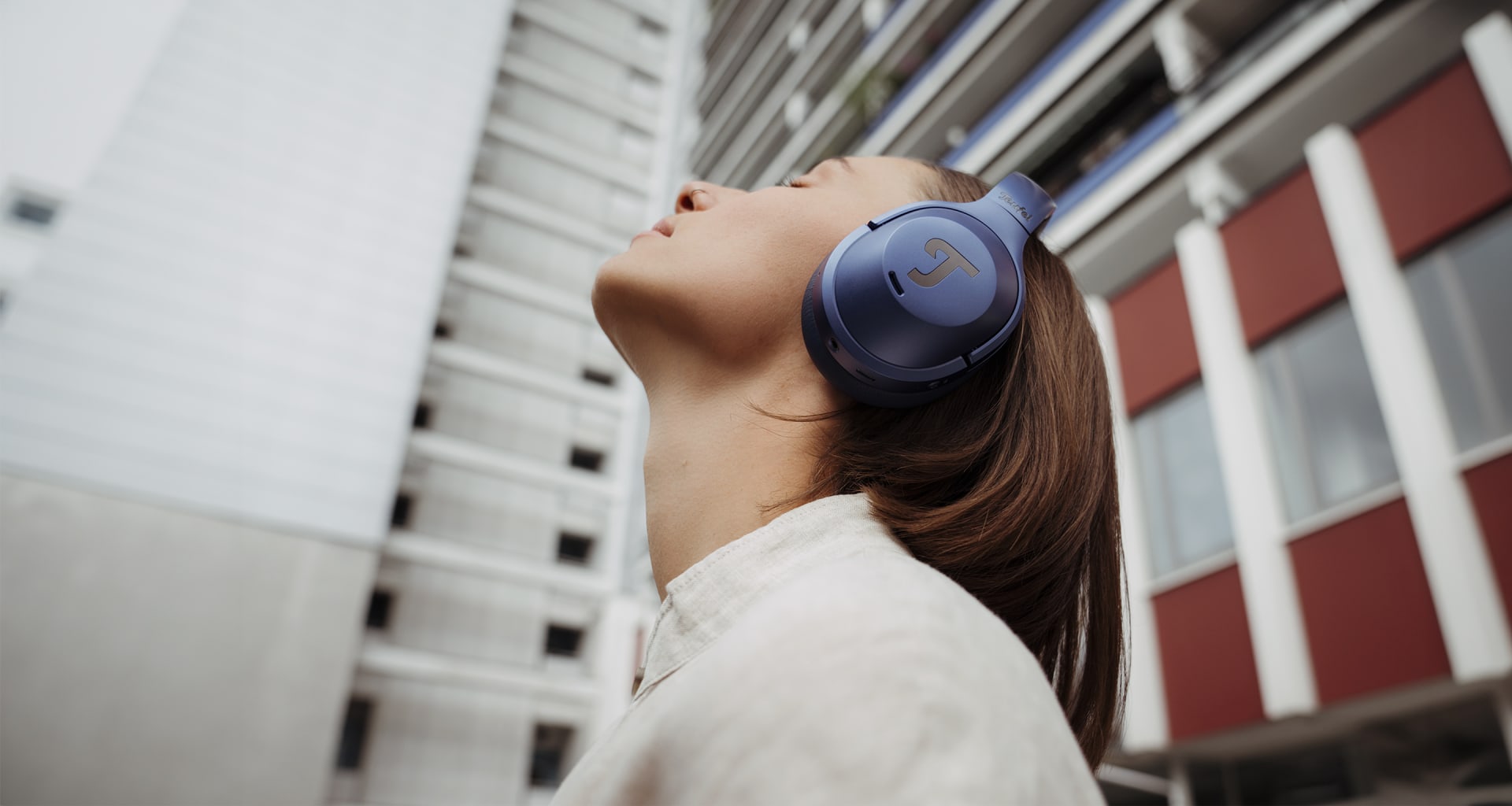 Junge Frau in Berlin mit dem REAL BLUE NC 3 in Steel Blue auf dem Kopf schaut nach oben und hört Musik