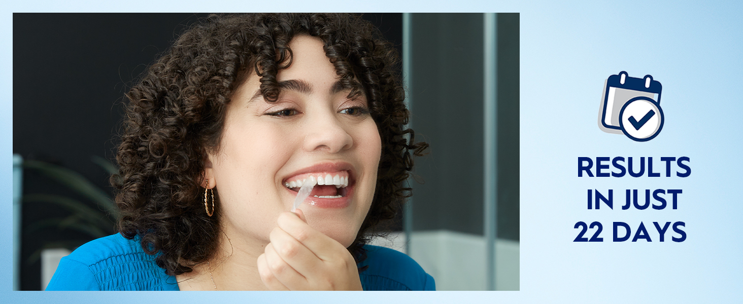 A woman smiles removing a Crest 3DWhitestrip off her top teeth. Claim reads: Results in just 22 days